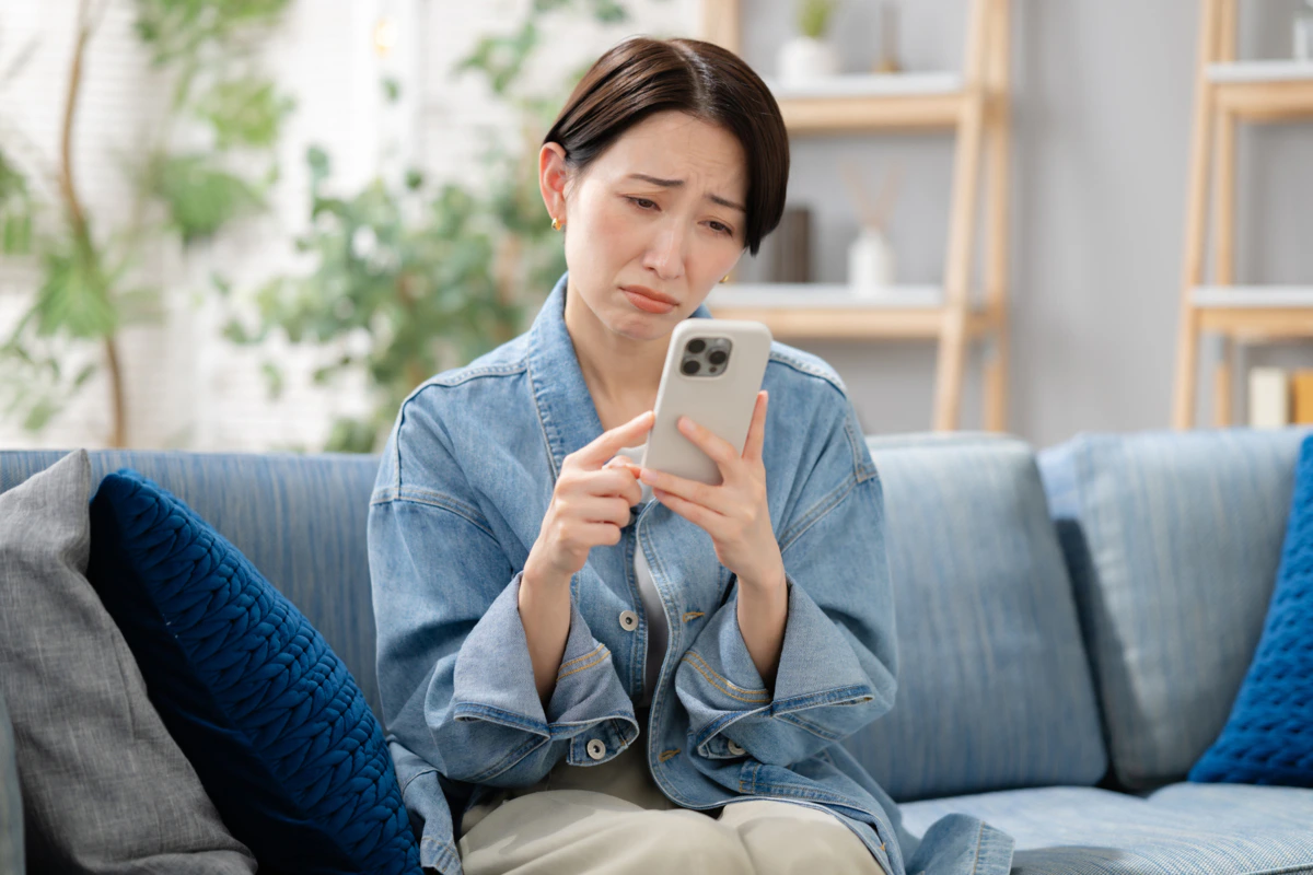 女性　困り顔　スマホ　ソファ